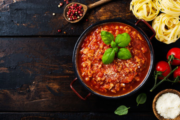 Traditional italian Bolognese sauce in saucepot an old dark wooden background. Top view, copy space