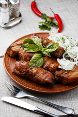 Grilled pork ribs in brown clay bowl close-up. Front view of plate with grilled pork ribs with onion and basil. Grey background. vertical photo. Top view
