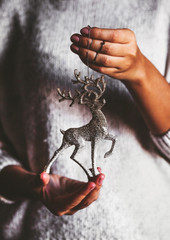 Woman in warm sweater holding toy deer glass decorative ball in hands, copy space. Christmas, new year holiday celebration concept