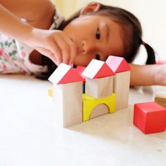 A little girl playing with colorful wooden blocks in the room. Child girl building house.