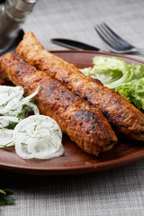 Shish kebab from ground beef meat. Lula kebab with white onion and salade, traditional Caucasian dish. Lined on a beautiful clay plate. vertical photo. grey background. top view.