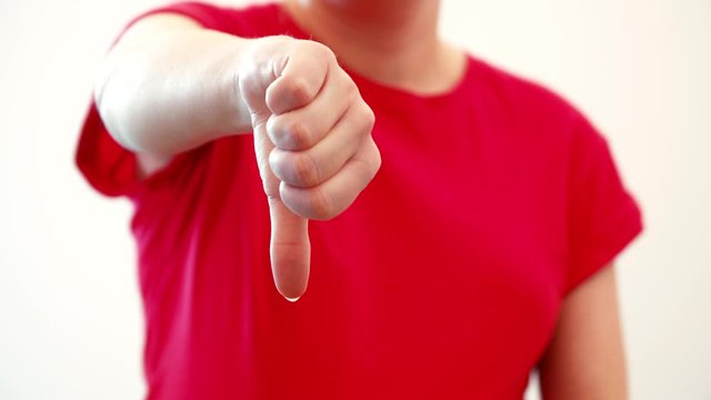 thumb down hand gesture sign. Woman in red against white background, static shot with soft focus