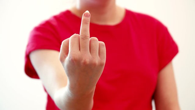Middle finger hand gesture from a woman in red t-shirt against white background. Shallow selective focus