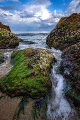 Fototapeta na wymiar Beautiful seascape with a close view of stones with moss and flowing water between. Vertical view