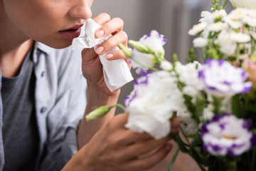 cropped view of woman with pollen allergy holding tissue and touching flowers