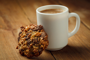 Cup with hot coffee milk and homemade backing chocolate cookies on a wooden table