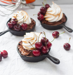 Chocolate tarts baked in mini iron skillets, with ganache filling and swiss meringue buttercream frosting, decorated with fresh cherries, on white background
