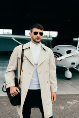 pensive stylish businessman in coat standing near plane