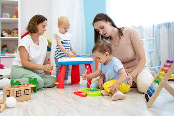 Kindergarten teacher playing with little kids in nursery. Developmental toys for preschool.