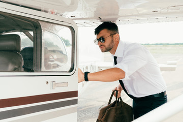 serious pilot in sunglasses holding bag near plane © LIGHTFIELD STUDIOS