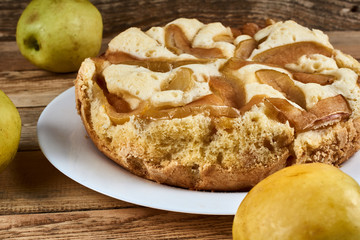 Baked apple pie on a white plate next to three green apples on a wooden background