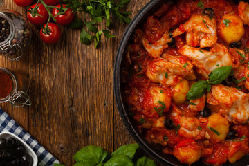 Traditionally prepared cod in Spanish. Served in tomato sauce with boiled potatoes, olivki and basil. Top view.