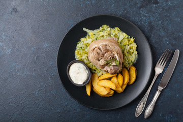 Boiled knuckle, served with cabbage and baked potatoes. Top view. Darkblue background. Dark mod.