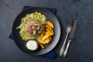 Boiled knuckle, served with cabbage and baked potatoes. Top view. Darkblue background. Dark mod.