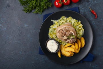 Boiled knuckle, served with cabbage and baked potatoes. Top view. Darkblue background. Dark mod.