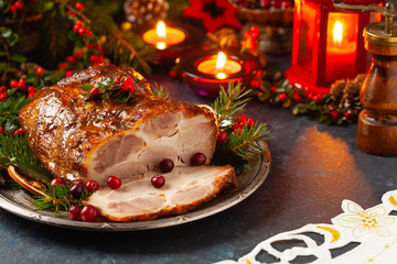 Roast pork neck in Christmas style. Dark navy blue background. Christmas accessories. Candles and lanterns in the background.