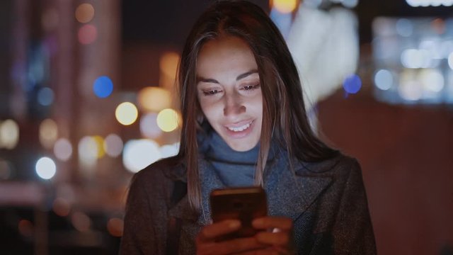 Closeup of prety smiling woman using smartphone walking at night city, slowmotion fullHD stock footage, handheld camera shot