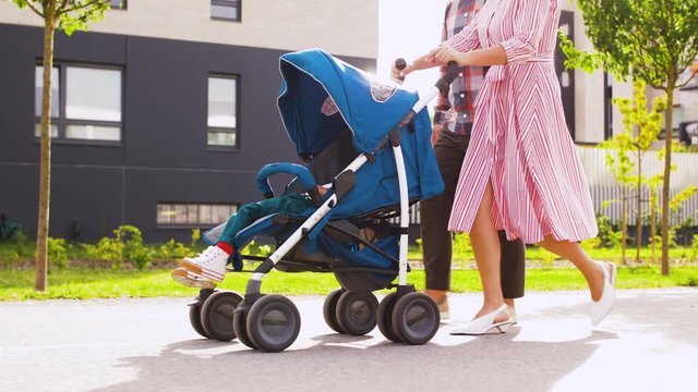 family, leisure and people concept - happy mother and father with little son in stroller walking along city street