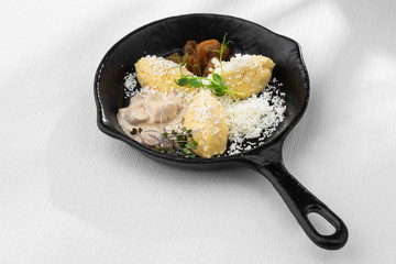 Typical Ukrainian dish polenta - Banosh with cheese, lard and white mushrooms. Maize porridge with bacon, cracklings and cheese. Corn porridge in black pan on white background. Horizontal photo.