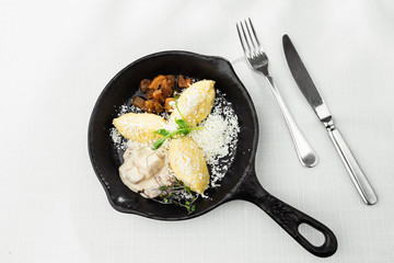 Typical Ukrainian dish polenta - Banosh with cheese, lard and white mushrooms. Maize porridge with bacon, cracklings and cheese. Corn porridge in black pan on white background. Horizontal photo.
