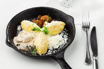 Typical Ukrainian dish polenta - Banosh with cheese, lard and white mushrooms. Maize porridge with bacon, cracklings and cheese. Corn porridge in black pan on white background. Horizontal photo.