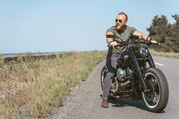 Fototapeta na wymiar Handsome bearded biker sitting on his motorcycle on the road