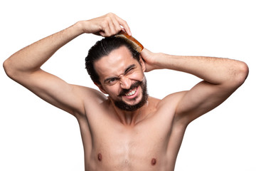 Fototapeta premium Stylish handsome bearded with mustaches have problems combing his hair standning bare isolated over white background. Concept of morning treatment. Morning routine