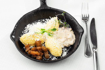 Typical Ukrainian dish polenta - Banosh with cheese, lard and white mushrooms. Maize porridge with bacon, cracklings and cheese. Corn porridge in black pan on white background. Horizontal photo.