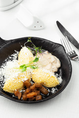 Typical Ukrainian dish polenta - Banosh with cheese, lard and white mushrooms. Maize porridge with bacon, cracklings and cheese. Corn porridge in black pan on white background. Vertical photo.