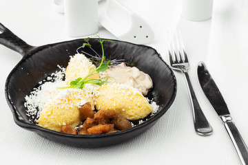 Typical Ukrainian dish polenta - Banosh with cheese, lard and white mushrooms. Maize porridge with bacon, cracklings and cheese. Corn porridge in black pan on white background. Horizontal photo.