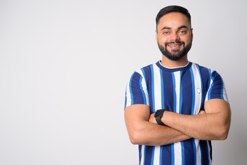 Portrait of happy young bearded Indian man smiling with arms crossed