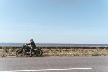 Fototapeta na wymiar Handsome muscular biker sitting on his bike looking over the ocean