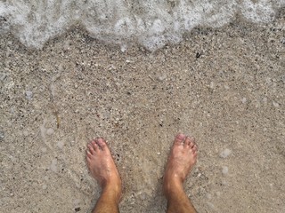 Man foots at seashore.Vacation on ocean beach, feet on sea sand, man walking barefoot in the sand in summer holidays on beach.