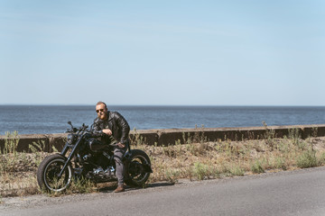 Handsome brutal man sitting on his motorcycle by the sea