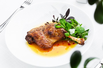 Roast duck leg with mango sauce, salade and chilli pepper on white plate, closeup. Horizontal view from above, top shot. White background.