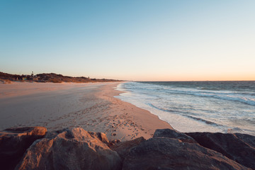 City beach at sunset. Golden light covers the sand and ocean while lighting up the sky. 