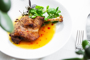 Roast duck leg with mango sauce, salade and chilli pepper on white plate, closeup. Horizontal view from above, top shot. White background.