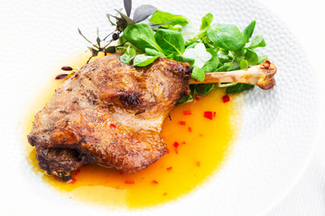 Roast duck leg with mango sauce, salade and chilli pepper on white plate, closeup. Horizontal view from above, top shot. White background.
