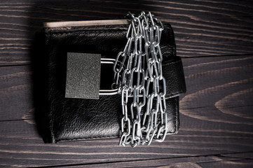 Leather wallet in chains with padlock on grey background.Business safety and finance protection concept - metal chain link with locked padlock on leather wallet full of dollar currency money.
