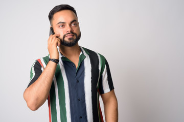 Portrait of young handsome bearded Indian man talking on the phone