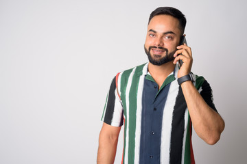 Portrait of happy young bearded Indian man talking on the phone