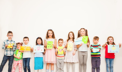 Happy kids showing their greeting card over white wall. Handmade paper crafts for kids
