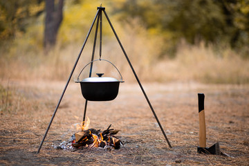 Campfire with camping tools such as axe and hanging pot over fire. Secluded relaxation in autumn...
