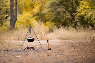 Campfire with camping tools such as axe and hanging pot over fire. Secluded relaxation in autumn...