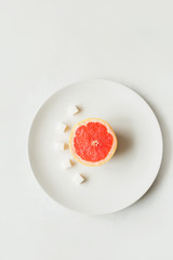 Half a grapefruit with sugar refined sugar on a white plate on a light background
