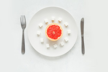 Half a grapefruit with sugar refined sugar on a white plate on a light background