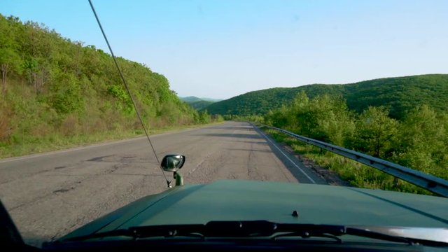 View from the front window of the car. A large green jeep rides along an asphalt country road with beautiful views. Car tourism.