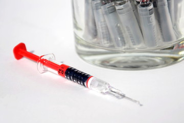 Red bright syringe lying on white background, diabetes, blood thinning or vaccination concept