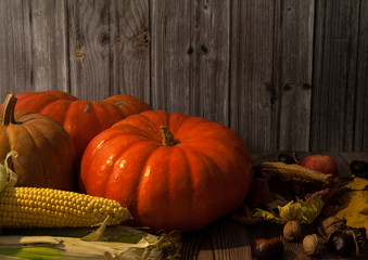Composition for Thanksgiving. Pumpkins, corn, apples, walnuts and chestnuts, autumn leaves on a wooden background.
