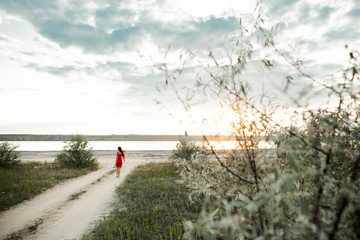 Silhouette of a beautiful girl in a red dress on the coast near the lake